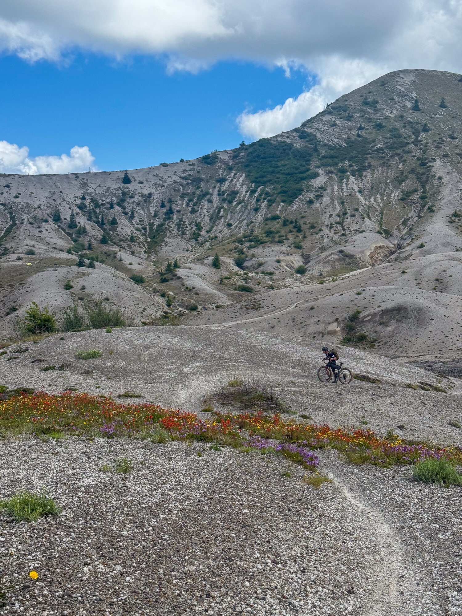 A tiny rider on a thread of trail below the vast eroded flank of the volcano
